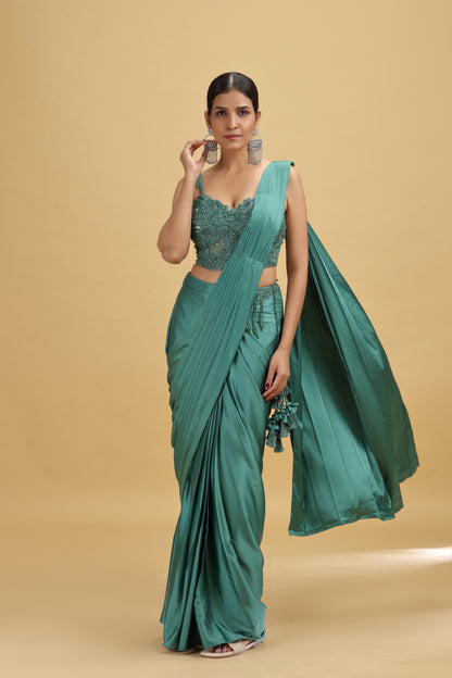 Woman wearing a green saree with a matching net blouse against a beige background