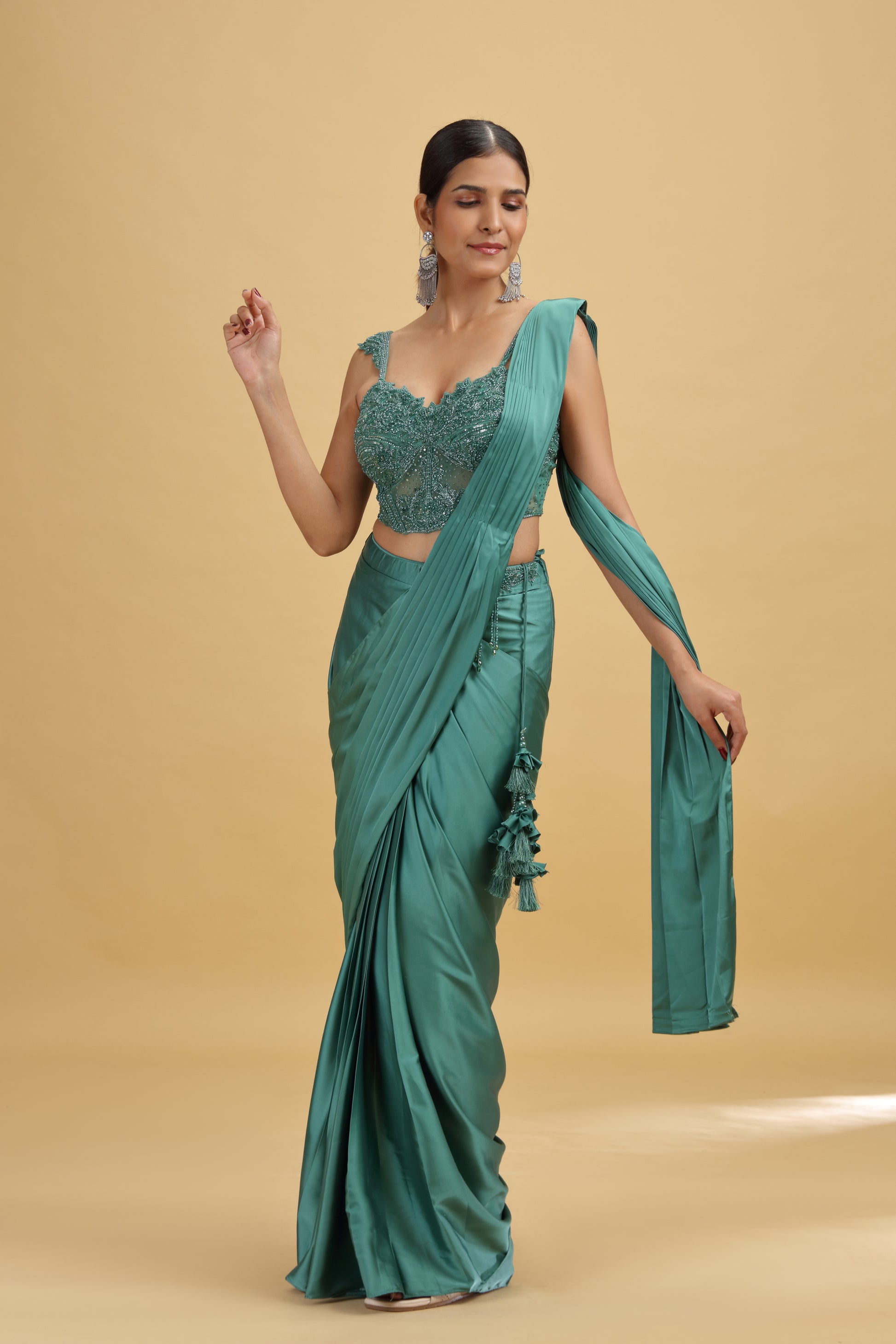 Woman wearing a green designer saree with a matching stitched net blouse on a beige background