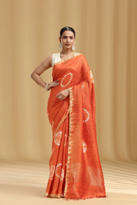 Woman wearing an rust orange saree with a white border against a beige background