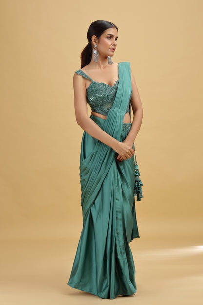 Woman wearing a green saree with a matching blouse against a beige background