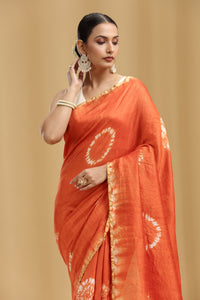 Woman wearing an rust orange silk saree with a beige background