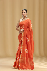 Woman wearing an orange saree with white patterns on a beige background