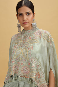 Woman wearing a light green embroidered outfit with tassels on a beige background