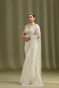 Woman wearing a white saree with a green curtain background