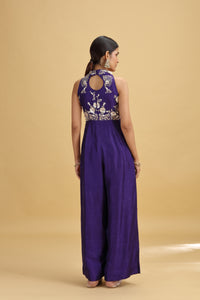 Woman wearing a purple jumpsuit with floral embroidery on a beige background