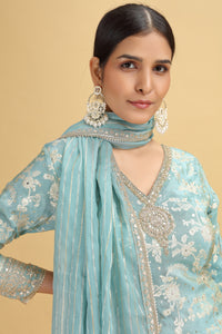 Woman wearing a light blue embroidered salwar suit with silver details on a beige background