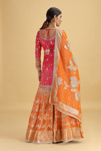 Woman wearing a traditional outfit with a pink blouse and orange dupatta on a beige background