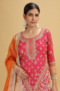 Woman wearing a pink and orange traditional outfit with intricate patterns on a beige background