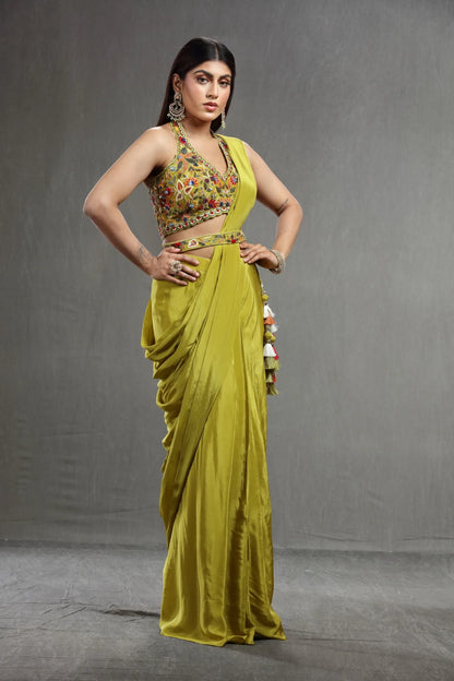 A woman in a vibrant olive saree with colorful embroidery on the blouse poses confidently.