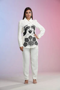 Woman wearing a white shirt with black floral design and white pants on a gradient background