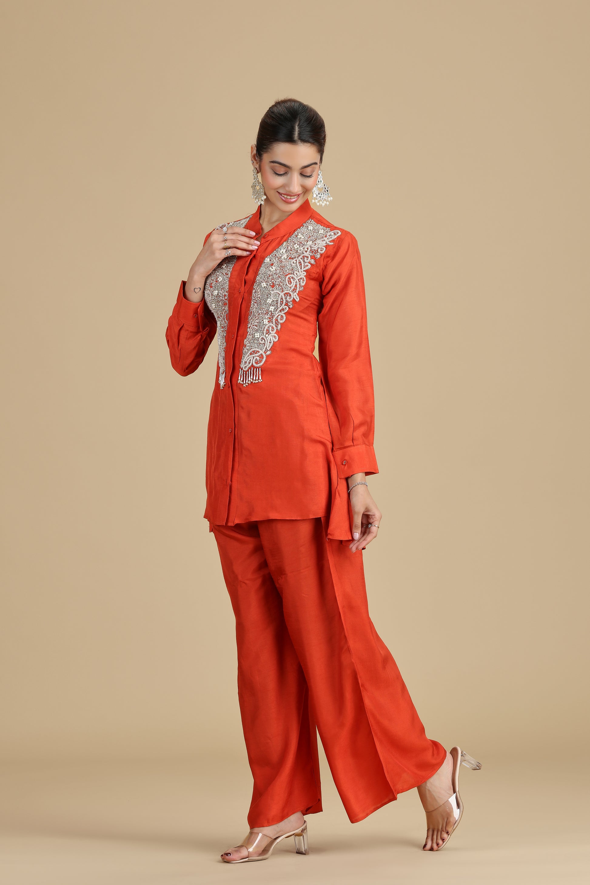 Woman wearing an orange traditional outfit with intricate embroidery on a beige background