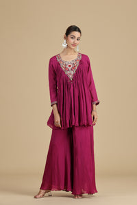 Woman wearing a magenta traditional outfit with intricate embroidery on a beige background