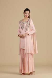 Woman wearing a pink traditional outfit with floral embroidery on a beige background