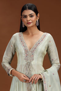 Woman wearing a light green traditional outfit with intricate embroidery on a brown background