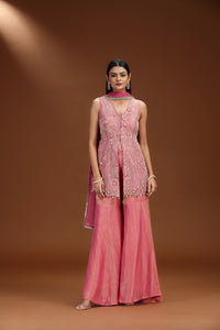 Woman wearing a pink traditional outfit with a matching dupatta against a brown background
