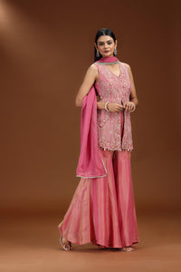 Woman in a traditional pink salwar suit outfit with embroidery on a brown background