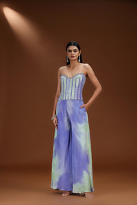 Woman wearing a strapless top and wide-leg pants with a tie-dye pattern on a brown background