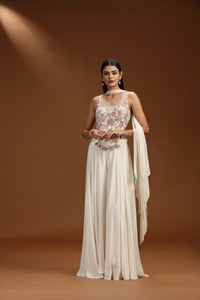 Woman in a floral top and white salwar suit with a brown background