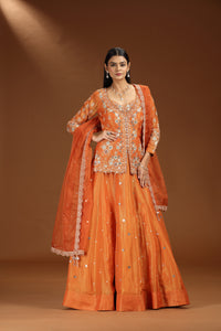 Woman wearing an orange satin silk lehenga with embroidery on a brown background