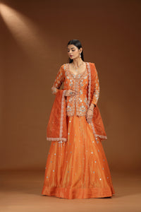 Woman wearing an orange satin silk lehenga with intricate designs on a brown background