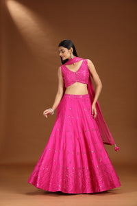 Woman wearing a bright pink lehenga set on a brown background