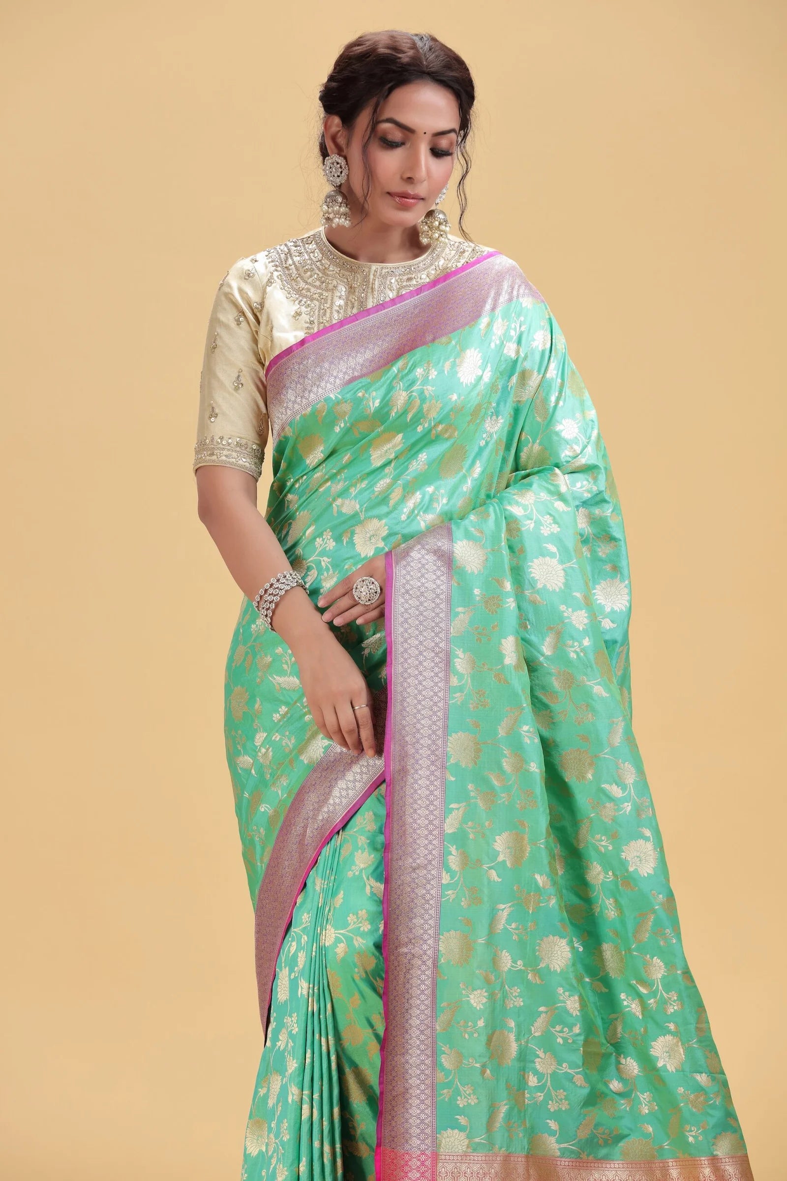 Woman wearing a green saree with a pink border on a beige background