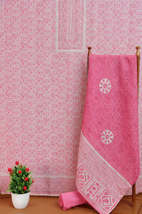 Pink fabric with white patterns on a wooden rod against a patterned fabric.