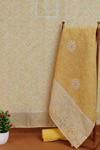 Golden fabric with white patterns draped over a wooden hanger against a patterned wall.