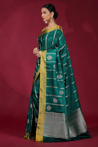 Woman wearing a green saree with gold border on a red background