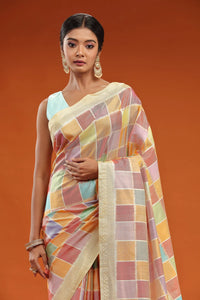 Woman wearing an elegant ivory-pink silk saree with intricate golden embroidery, posing indoors.
