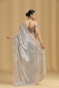 Woman wearing a silver saree with a beige background