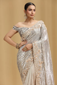 Woman wearing a silver saree with floral embellishments on a beige background