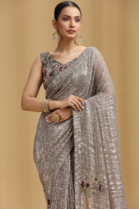 Woman wearing a mouse grey net saree with floral embellishments on a beige background