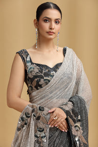 Woman wearing a black floral blouse with a silver saree against a beige background