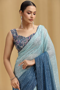 Woman wearing a blue net saree with a floral blouse against a beige background