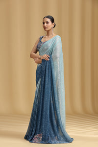 Woman wearing a Sea Green & Royal Blue Net Saree with a light blue blouse against a beige background