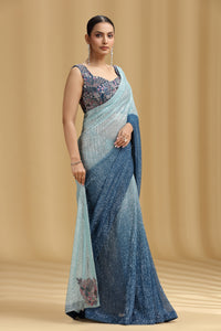 Woman wearing a sea green and light blue net saree with a beige background