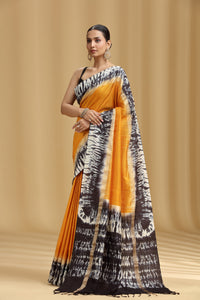 Woman wearing a black, white, and orange saree against a beige background