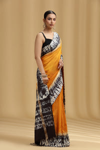 Woman wearing a black, white, and orange saree against a beige background