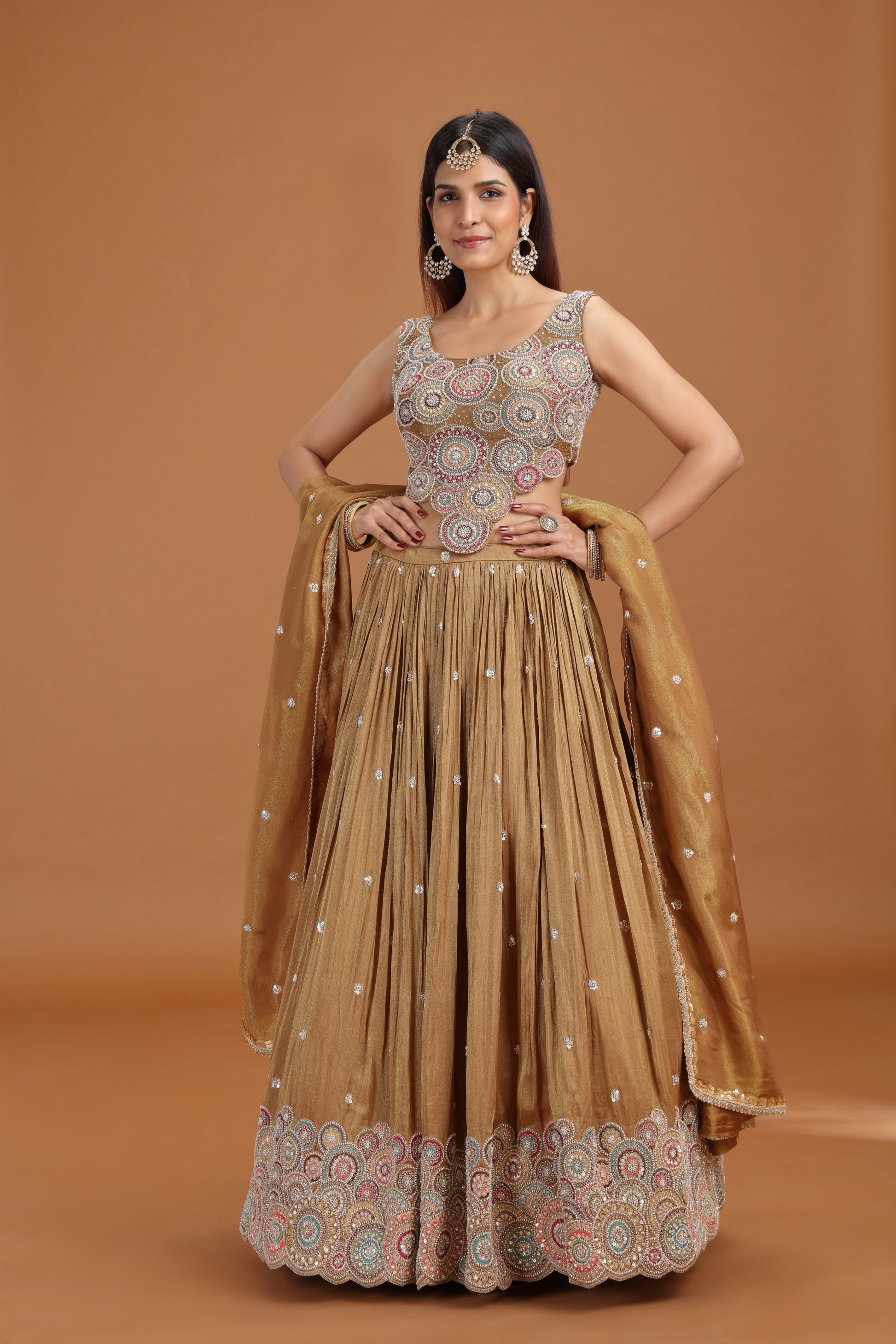 Woman posing in a dusty gold tissue lehenga with aari pearl work 