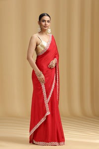 Woman wearing a red saree with golden blouse against a beige background