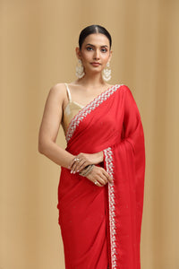 Woman wearing a red saree with white border against a beige background