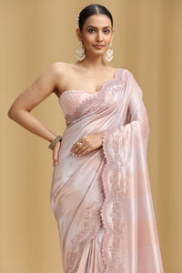 Woman wearing a pink tissue saree with intricate designs on a beige background