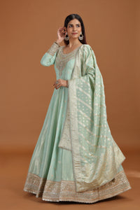 Woman wearing a light green traditional outfit with a matching dupatta on a brown background