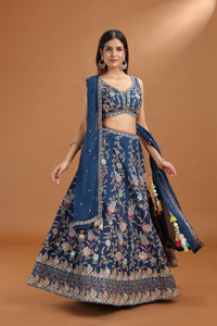 Woman wearing a blue floral lehenga with a matching dupatta on a brown background