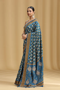 Woman wearing a blue and gold saree with a geometric pattern on a beige background