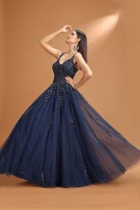 Woman wearing a navy blue evening gown with intricate detailing on a brown background