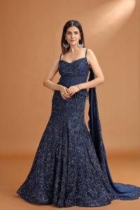 Woman wearing a navy blue evening gown with a cape against a brown background