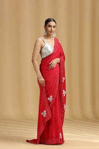 Woman wearing a red satin silk saree with white patterns on a beige background