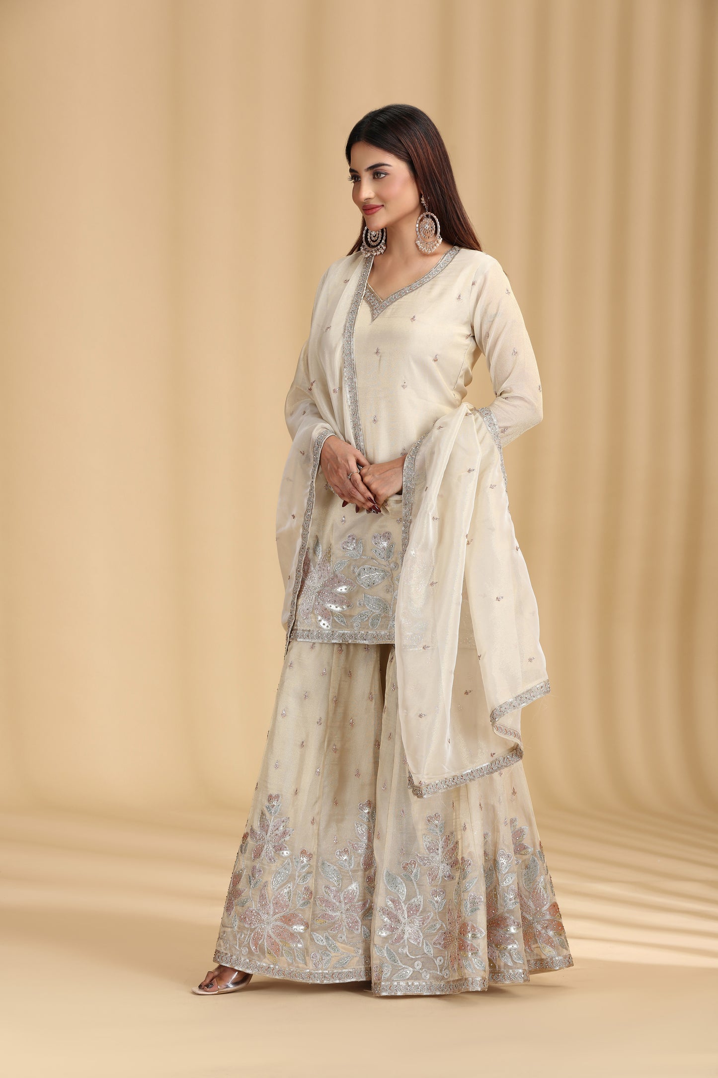 Woman wearing a traditional outfit with a beige and silver dupatta against a beige background
